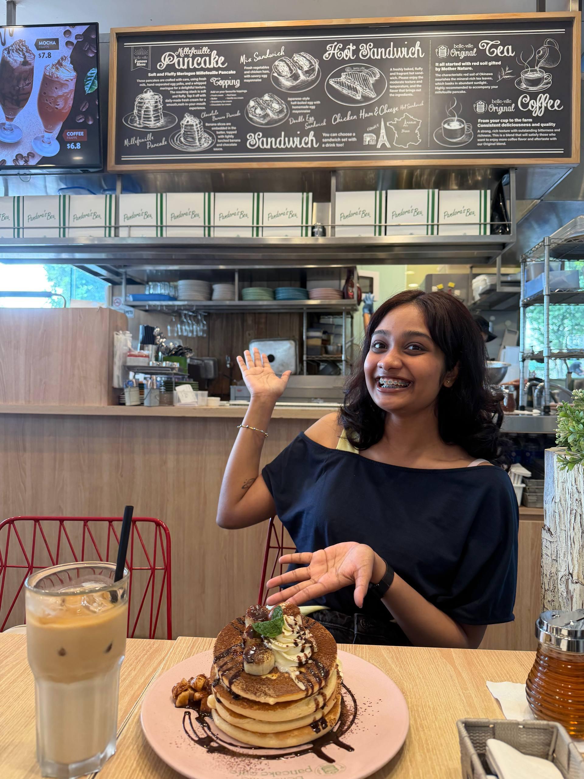 Esha Nakka smiling at a café table with pancakes and coffee